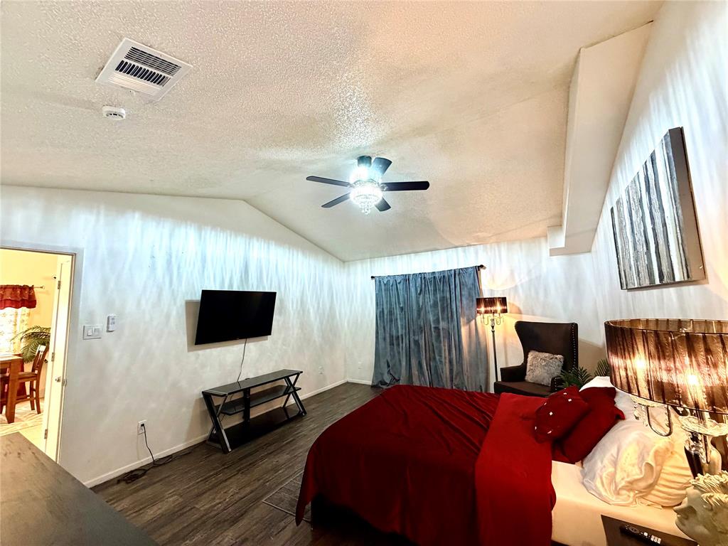 Vaulted ceiling bedroom featuring wood-finish flooring, a ceiling fan with integrated lighting, and a wall-mounted television Vaulted ceiling bedroom featuring wood-finish flooring, a ceiling fan with integrated lighting, and a wall-mounted television