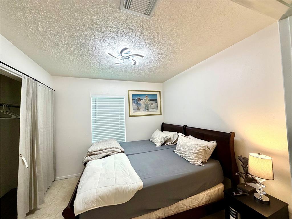 Bedroom featuring a window with horizontal blinds, overhead flush-mount lighting, and a closet with a curtain closure