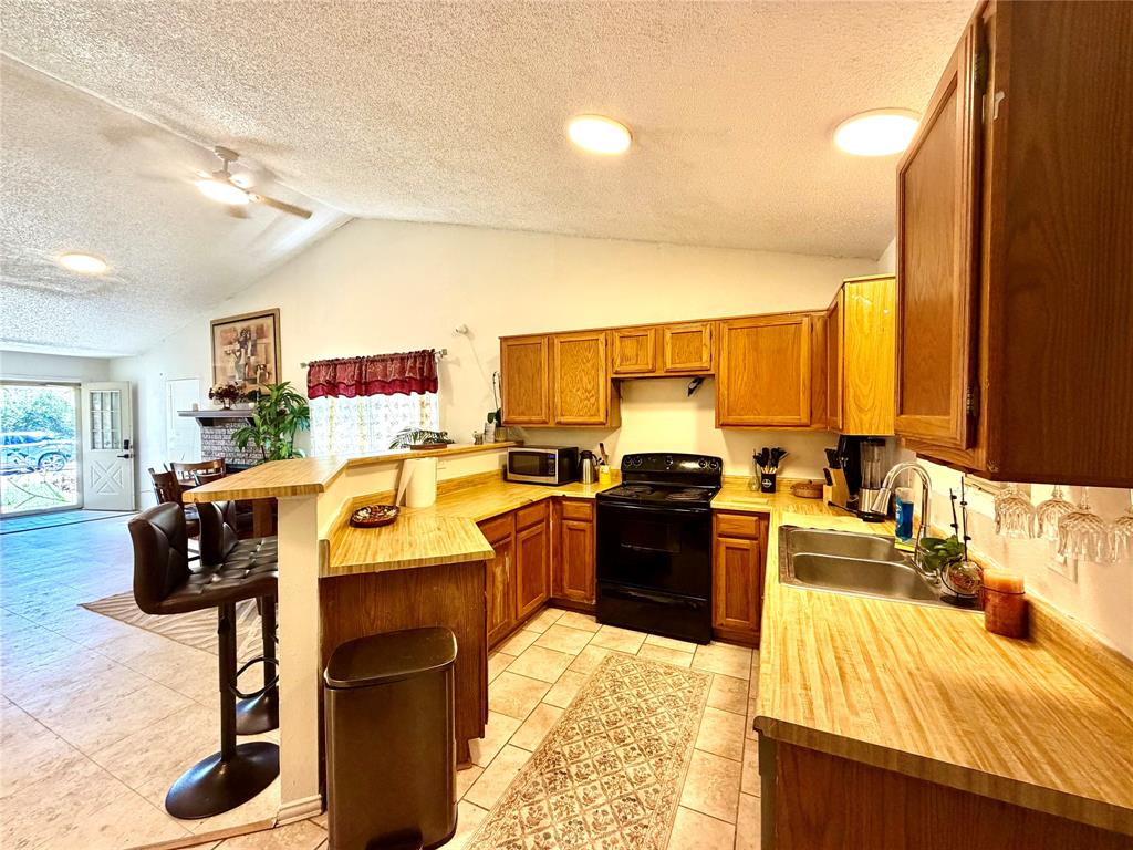 Open-concept kitchen featuring wood-finish cabinetry, light wood-finish countertops, and a black appliance suite Open-concept kitchen featuring wood-finish cabinetry, light wood-finish countertops, and a black appliance suite