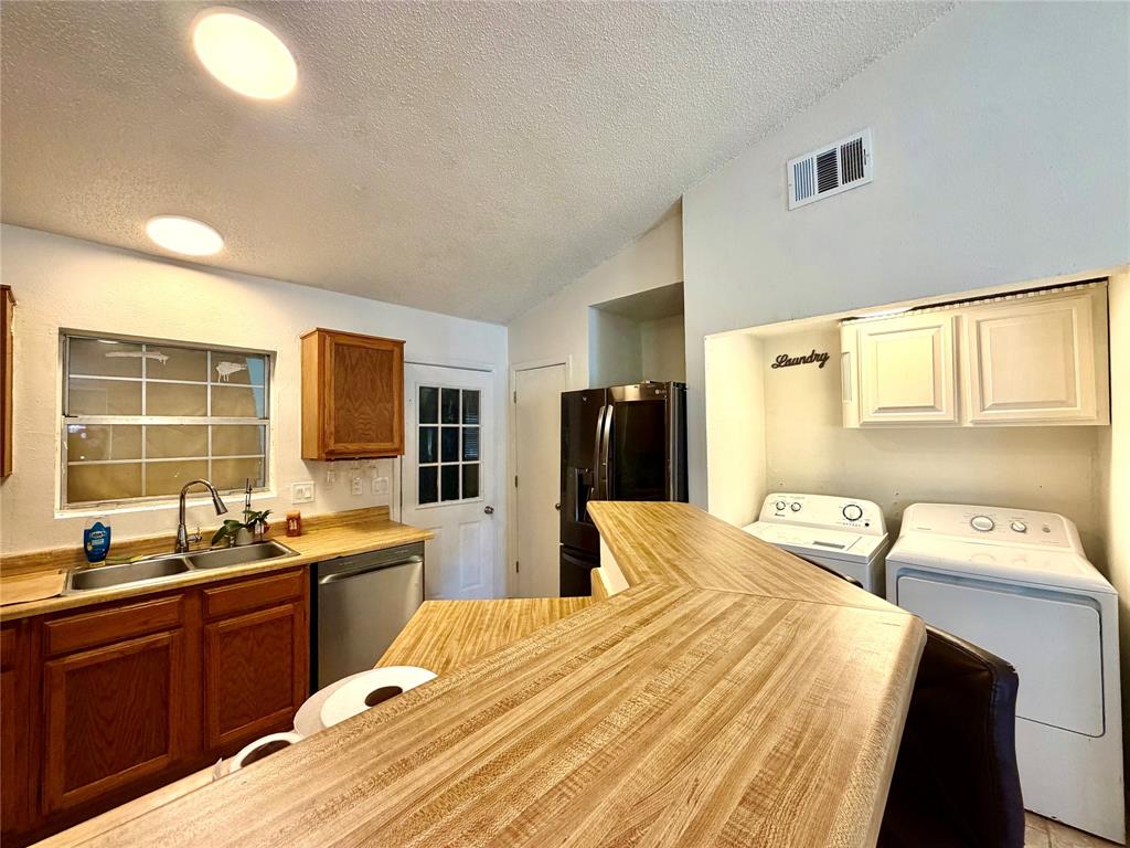 Kitchen area featuring a wood-finish countertop bar, stainless steel sink, wood cabinetry, and a full-light rear door Kitchen area featuring a wood-finish countertop bar, stainless steel sink, wood cabinetry, and a full-light rear door
