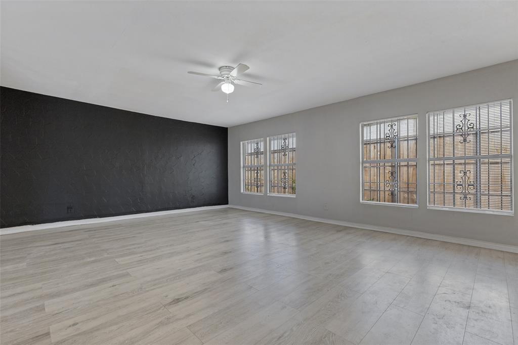 Interior space featuring wood-finish flooring, a textured accent wall, four windows with exterior security bars, and a ceiling fan with integrated lighting