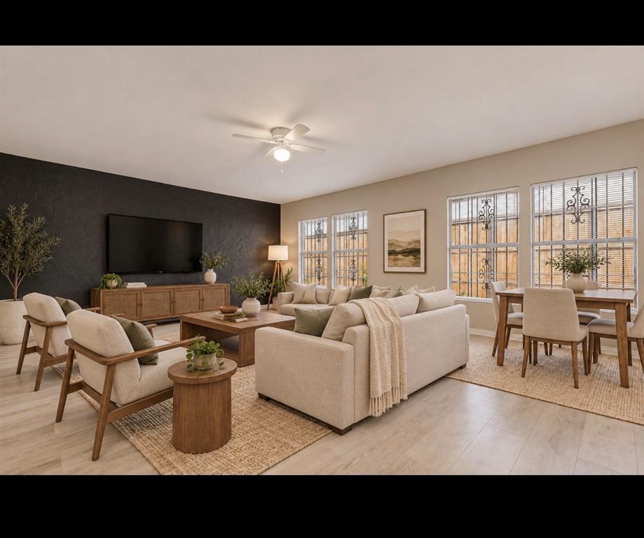 Open-concept living space featuring wood-finish flooring, a charcoal-toned accent wall, and multiple windows with iron security bars, finished with a central ceiling fan *virtually staged*