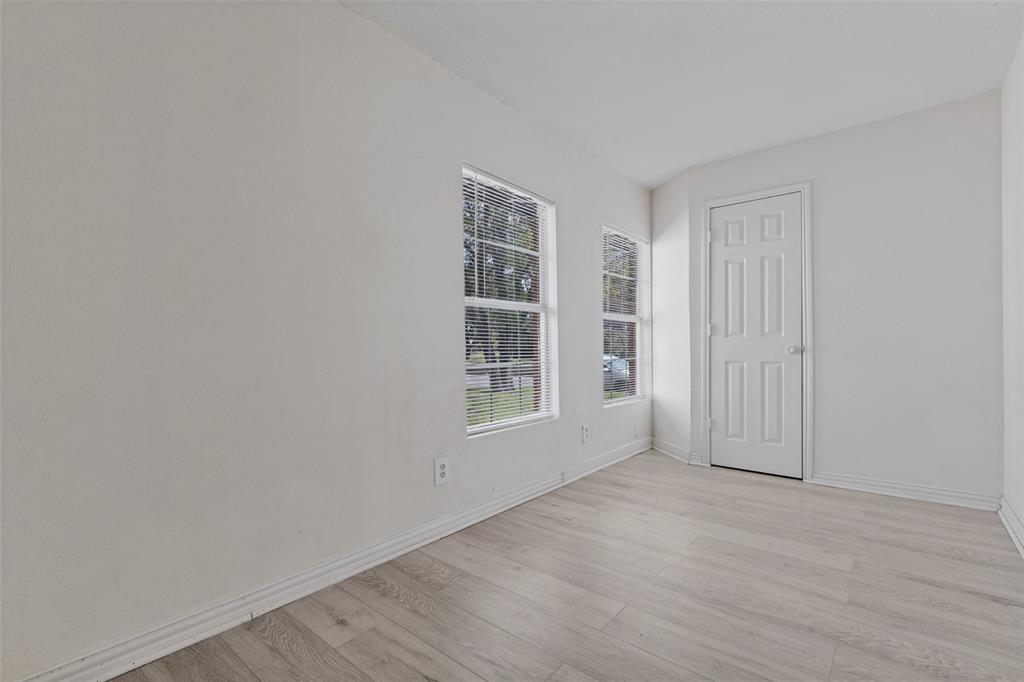 Neutral-toned interior space featuring light-colored wood-finish flooring, two large windows, and a six-panel door