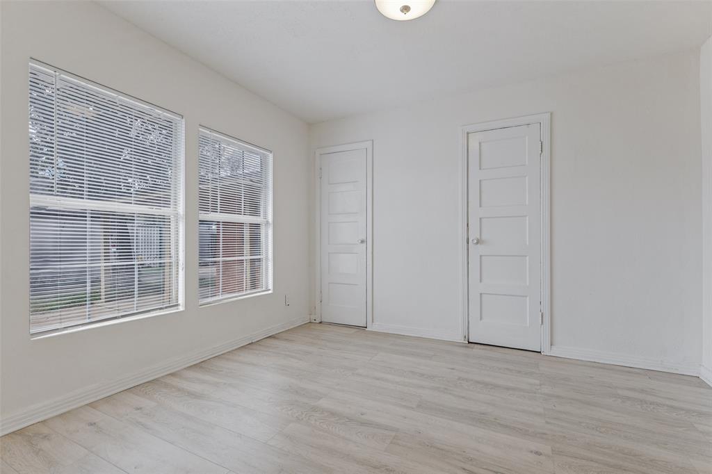 Neutral-toned interior space featuring wood-finish flooring, two dual-pane windows with integrated blinds, and two classic five-panel interior doors