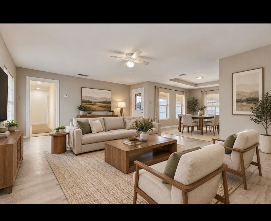 Open-concept interior featuring light wood-finish flooring, recessed lighting, neutral wall paint, and a tray ceiling- *virtually staged*