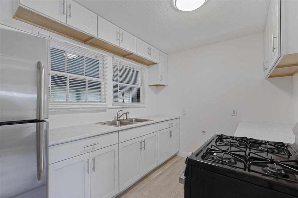 Kitchen featuring white shaker-style cabinetry, stainless steel appliances, double-basin sink with a gooseneck faucet, and light-toned wood-finish flooring