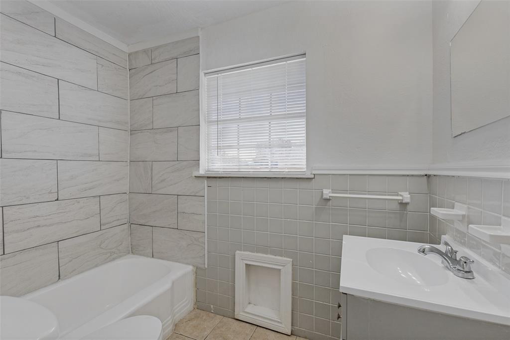 Bathroom featuring a tub with large-format wall tile, square wall-tile surround, vanity with an integrated sink, polished metal hardware, and a wall-mounted towel bar