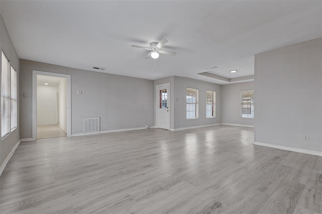 Neutral-toned interior space featuring wood-finish flooring, a tray ceiling, multiple windows, and a ceiling fan with integrated light fixture
