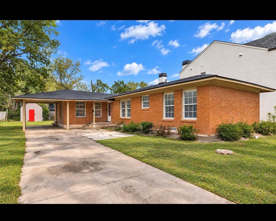Single-story brick exterior featuring a covered carport, asphalt shingle roof, multi-pane windows, and a concrete driveway