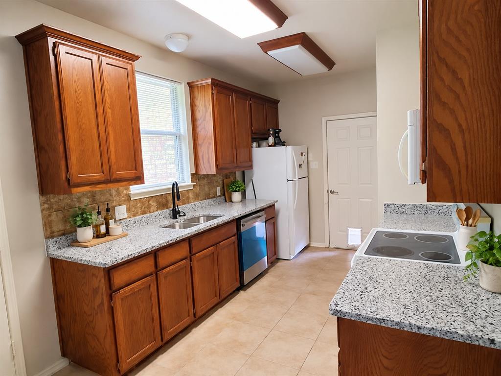 Kitchen featuring wood cabinetry, stone-finish countertops, tile backsplash, tile flooring, and integrated dishwasher Kitchen featuring wood cabinetry, stone-finish countertops, tile backsplash, tile flooring, and integrated dishwasher