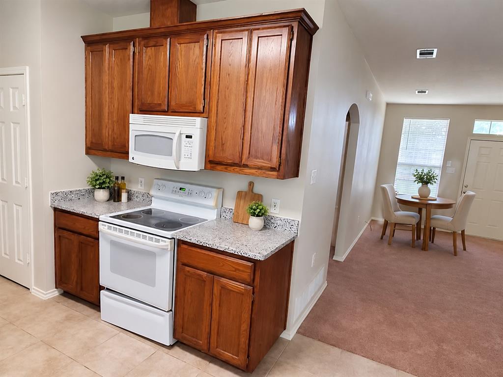 Kitchen featuring stained wood cabinetry, speckled stone-finish countertops, and white appliances including a built-in microwave and electric range Kitchen featuring stained wood cabinetry, speckled stone-finish countertops, and white appliances including a built-in microwave and electric range