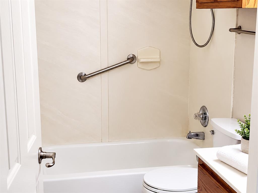 Bathroom featuring a tub-shower combination with integrated wall surrounds, brushed metal grab bar, built-in soap dish, and a vanity with a white countertop Bathroom featuring a tub-shower combination with integrated wall surrounds, brushed metal grab bar, built-in soap dish, and a vanity with a white countertop