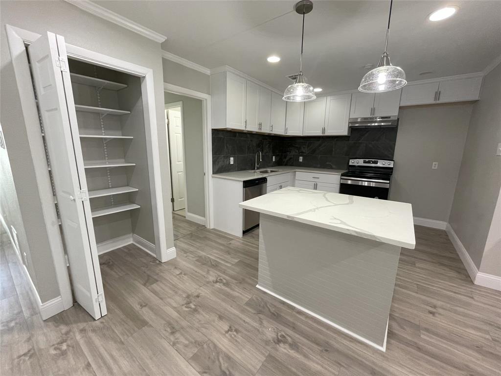 Kitchen with appliances with stainless steel finishes, light hardwood / wood-style flooring, tasteful backsplash, white cabinets, and a center island