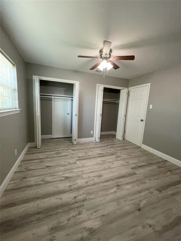Unfurnished bedroom featuring multiple closets, ceiling fan, and hardwood / wood-style flooring