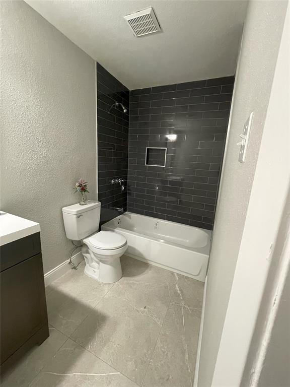 Full bathroom with toilet, tile patterned floors, tiled shower / bath combo, and vanity