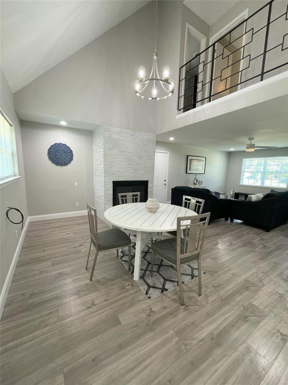 Dining room featuring high vaulted ceiling, a fireplace, light wood-type flooring, and a notable chandelier