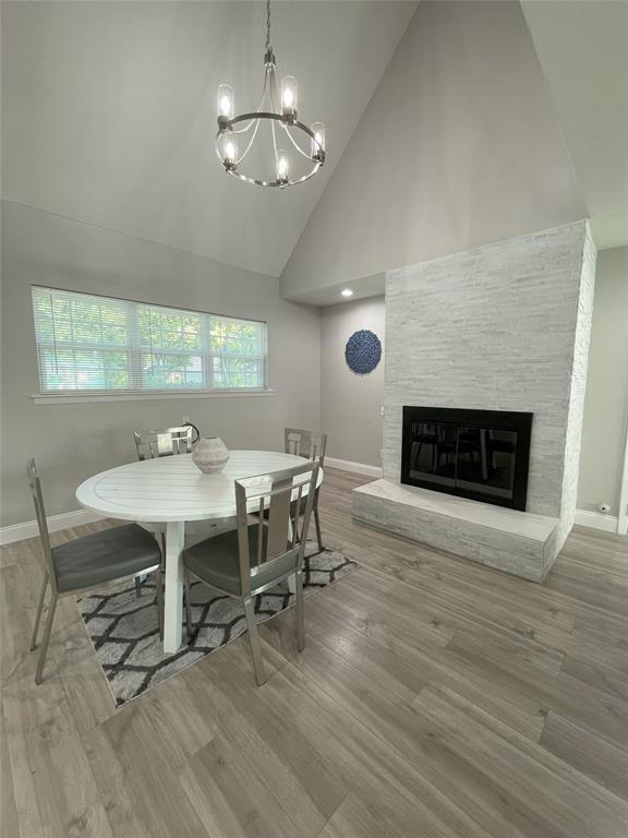 Dining area featuring a wealth of natural light, an inviting chandelier, a fireplace, hardwood / wood-style flooring, and high vaulted ceiling