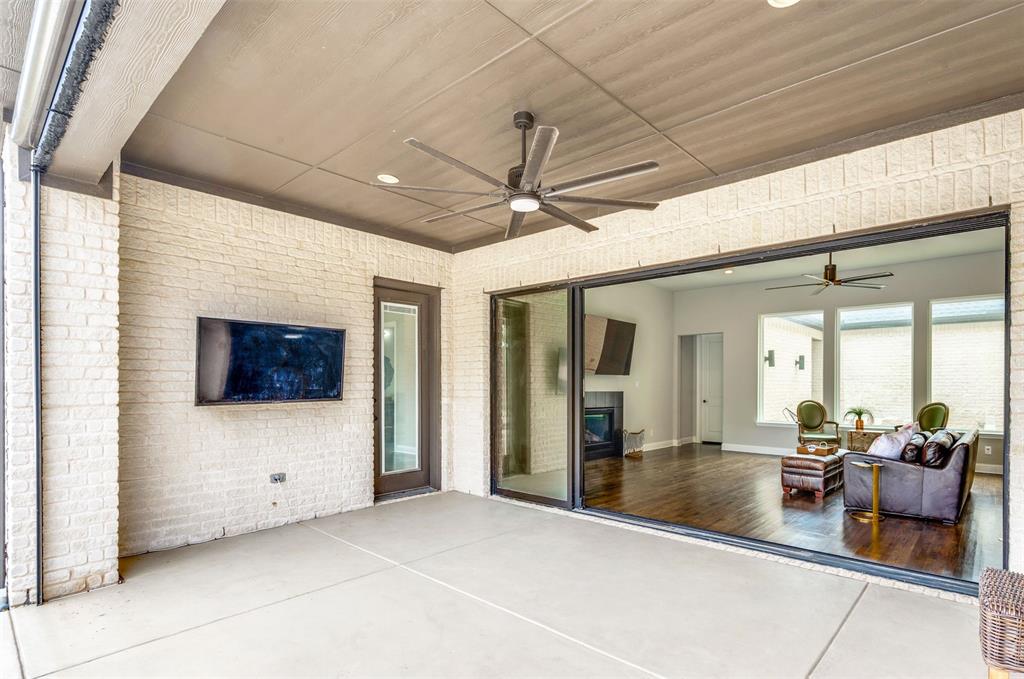 Covered patio with a concrete slab, white brick exterior walls, and a dark ceiling fan