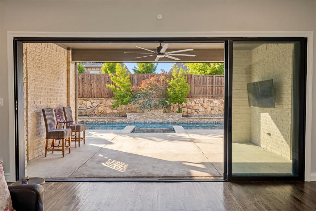 Glass sliding wall leads to expansive outdoor living area featuring a covered patio, swimming pool, and concrete decking.
