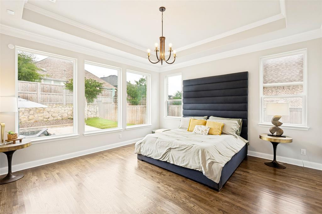 Spacious primary suite room featuring wood flooring, a tray ceiling with a central chandelier and great views of the backyard oasis.