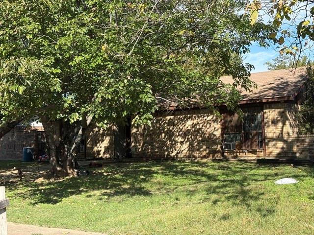Single-story residence featuring a brick facade, asphalt shingle roof, and mature trees on the lot
