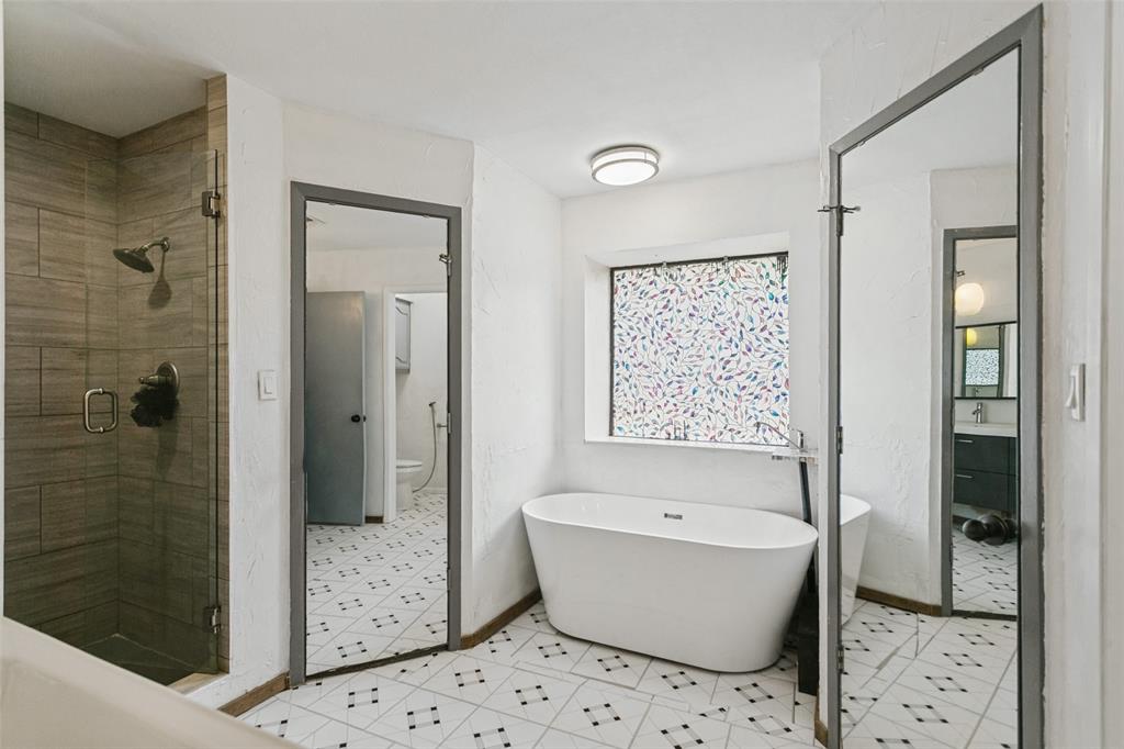 Freestanding soaking tub, walk-in shower with wood-finish tile surround, glass shower enclosure, and patterned tile flooring