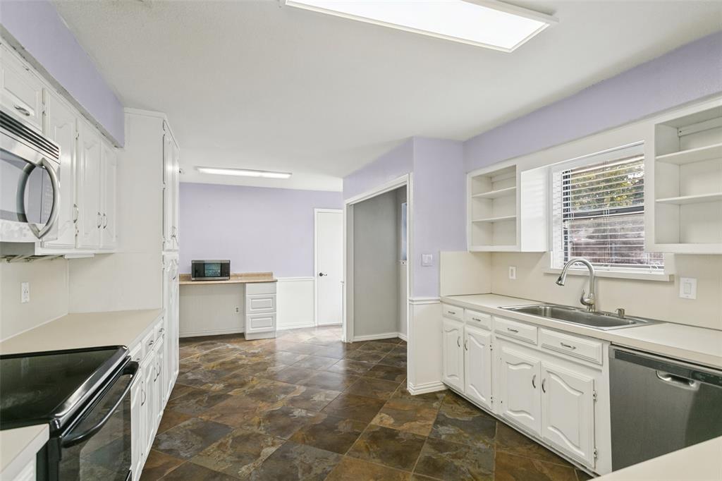 Kitchen featuring white cabinetry, solid-surface countertops, stone-finish tile flooring, built-in shelving, and a stainless steel kitchen faucet Kitchen featuring white cabinetry, solid-surface countertops, stone-finish tile flooring, built-in shelving, and a stainless steel kitchen faucet