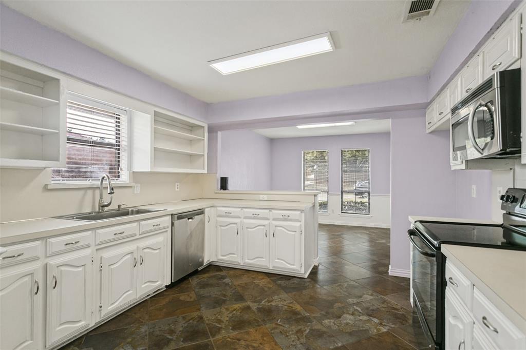 Kitchen featuring white cabinetry with raised-panel doors, solid surface countertops, stainless steel dishwasher, integrated microwave, and tile flooring