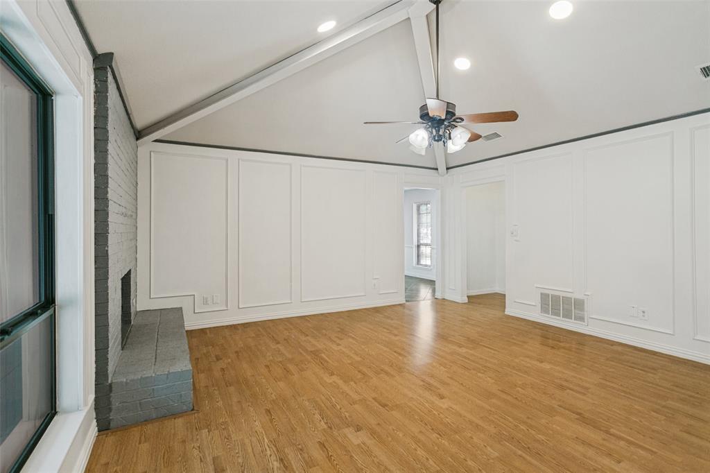 Vaulted ceiling with exposed structural beams, wood-finish flooring, painted brick fireplace, and wall paneling detail Vaulted ceiling with exposed structural beams, wood-finish flooring, painted brick fireplace, and wall paneling detail