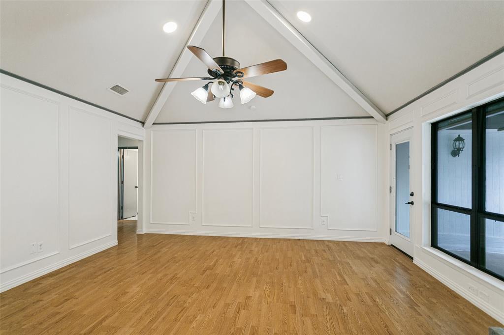 Vaulted ceiling featuring exposed beams, wood-finish flooring, wainscoting wall detailing, and a multi-light ceiling fan Vaulted ceiling featuring exposed beams, wood-finish flooring, wainscoting wall detailing, and a multi-light ceiling fan