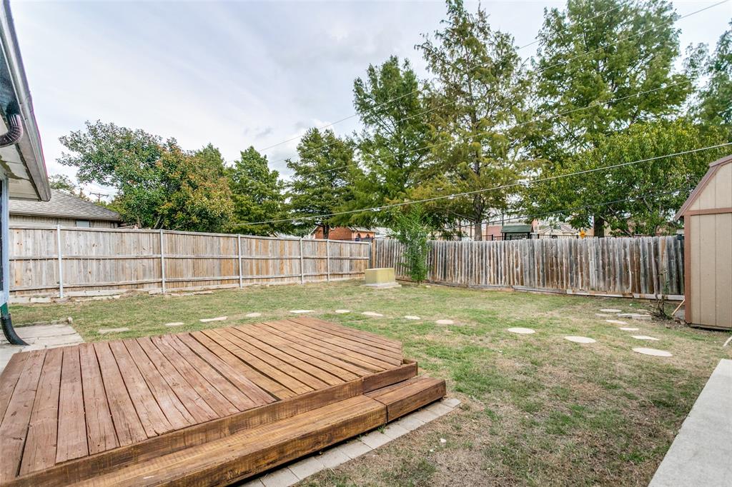 Backyard featuring a tiered wooden deck, perimeter wood fencing, mature trees, and stone paver path