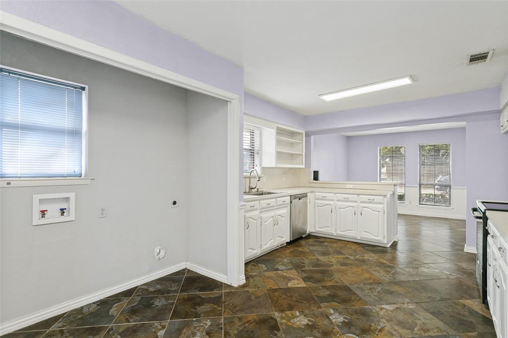 Kitchen featuring white cabinetry, integrated dishwasher, stainless steel sink with pull-down faucet, stone-tile flooring, and dedicated laundry hookups