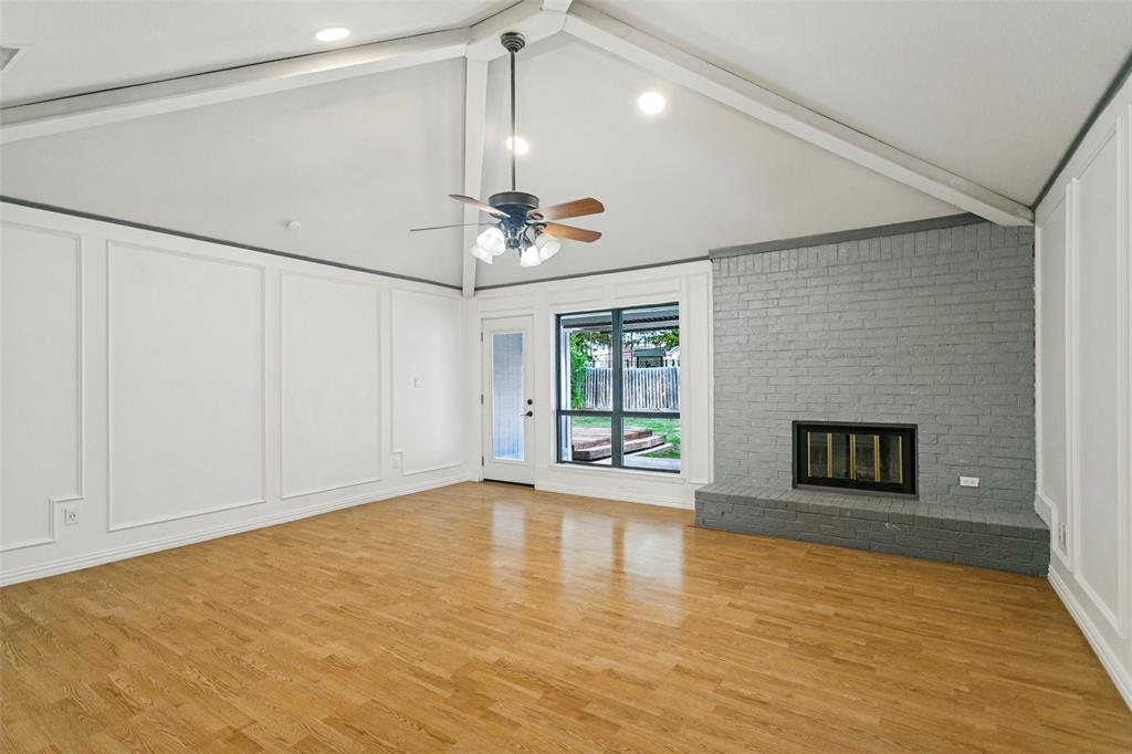Vaulted ceiling with exposed beams, wood-finish flooring, floor-to-ceiling wainscoting, and a painted brick fireplace with an elevated hearth Vaulted ceiling with exposed beams, wood-finish flooring, floor-to-ceiling wainscoting, and a painted brick fireplace with an elevated hearth