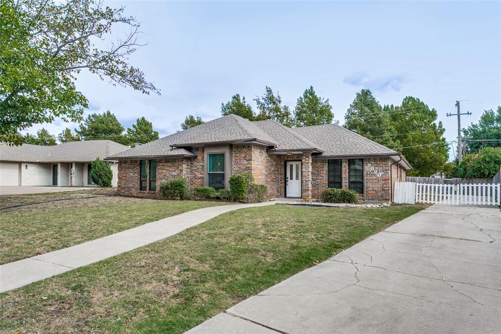 Single-story brick exterior featuring a hip roof, concrete driveway, and white picket fencing Single-story brick exterior featuring a hip roof, concrete driveway, and white picket fencing