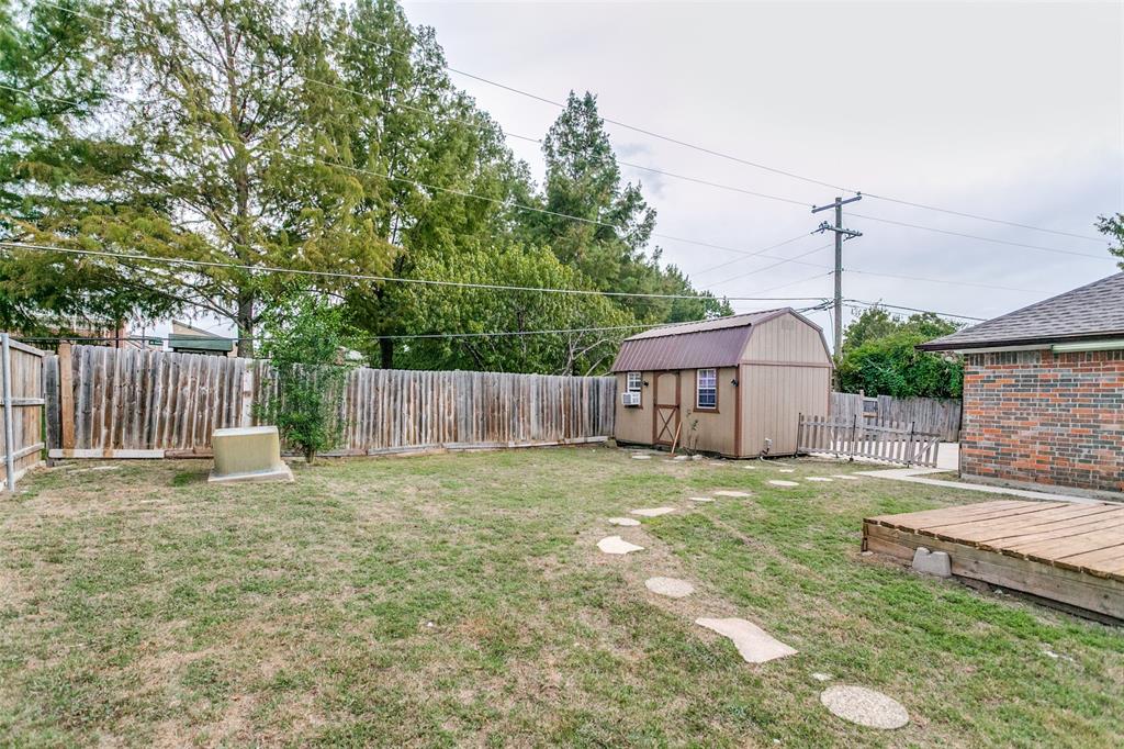 Backyard featuring a wood-style shed, natural stone paver pathway, brick exterior siding, and a wooden ground-level deck, enclosed by perimeter wood fencing