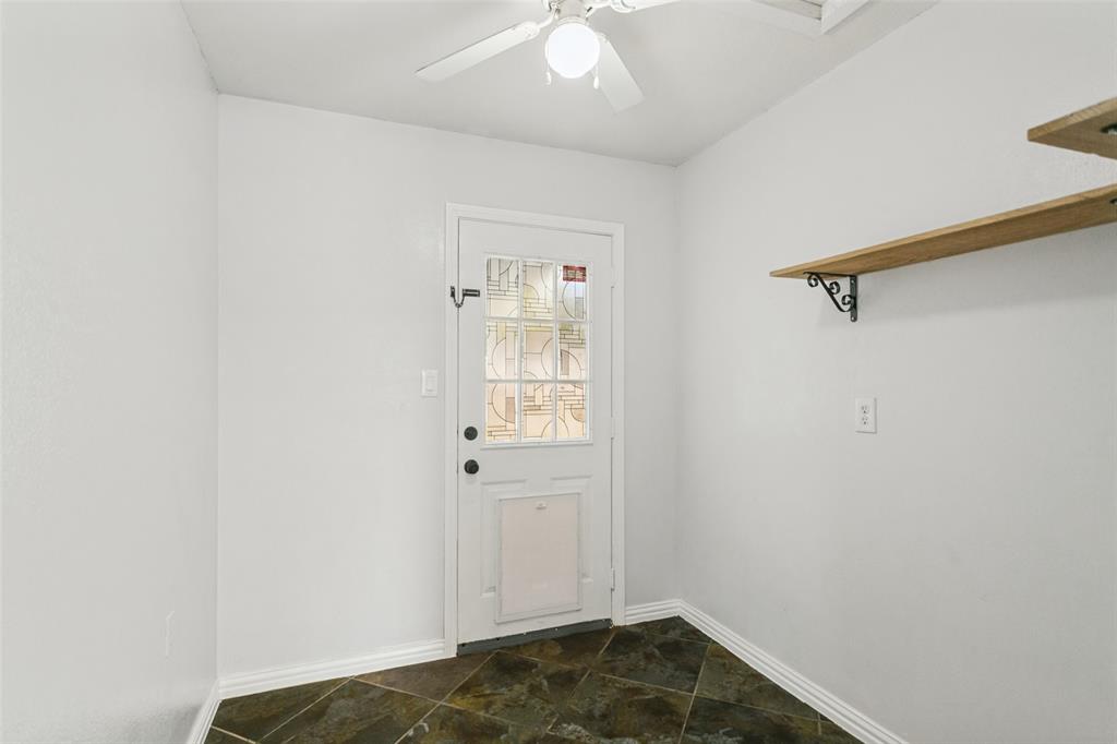 Entryway featuring diagonal slate flooring, a white door with a decorative glass panel, integrated pet door, and wall-mounted wood shelving with decorative metal brackets, complemented by a ceiling fan with integrated lighting