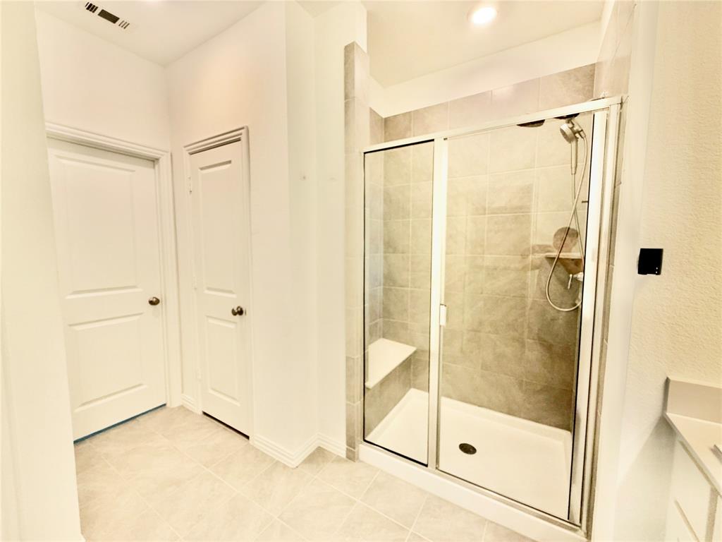 Walk-in shower featuring a glass enclosure, built-in bench seat, ceramic tile surround, and handheld shower fixture, complemented by neutral tile flooring