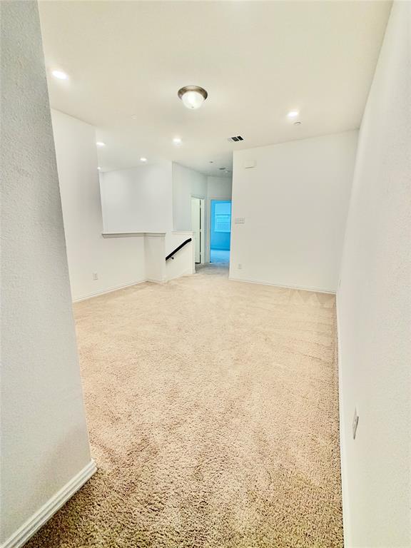 Neutral-toned carpeting, recessed ceiling lighting, a flush-mount light fixture, and a stairwell with a fixed handrail