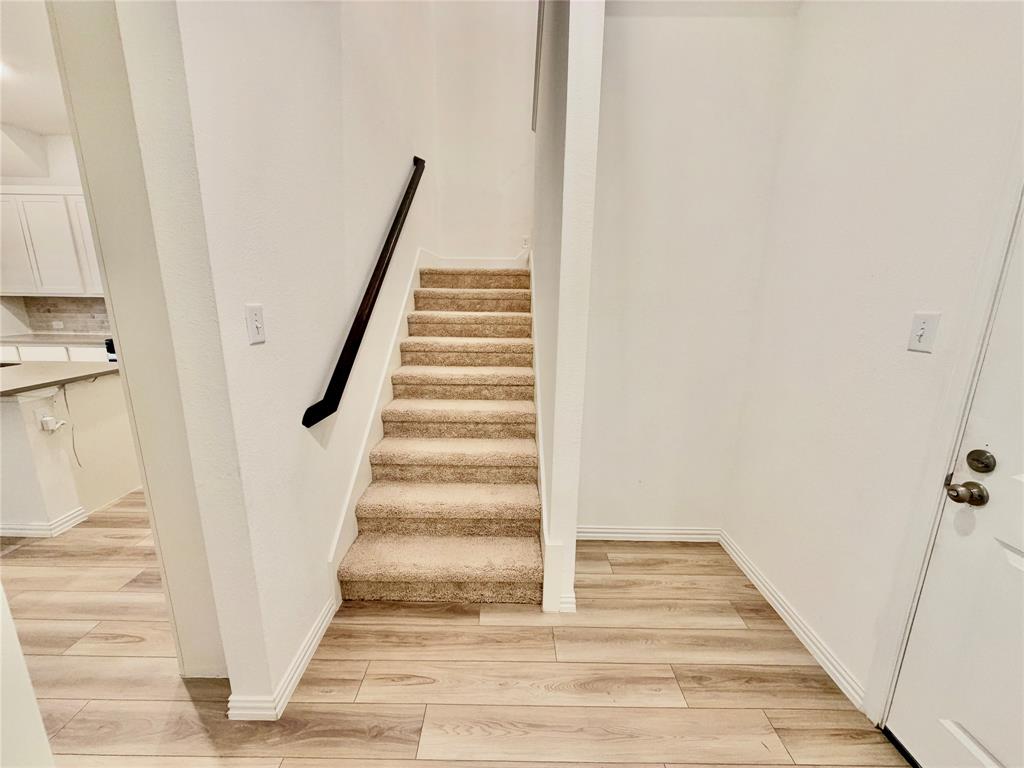 Staircase featuring wall-to-wall carpeting and a matte black handrail, set against neutral walls with wood-finish flooring