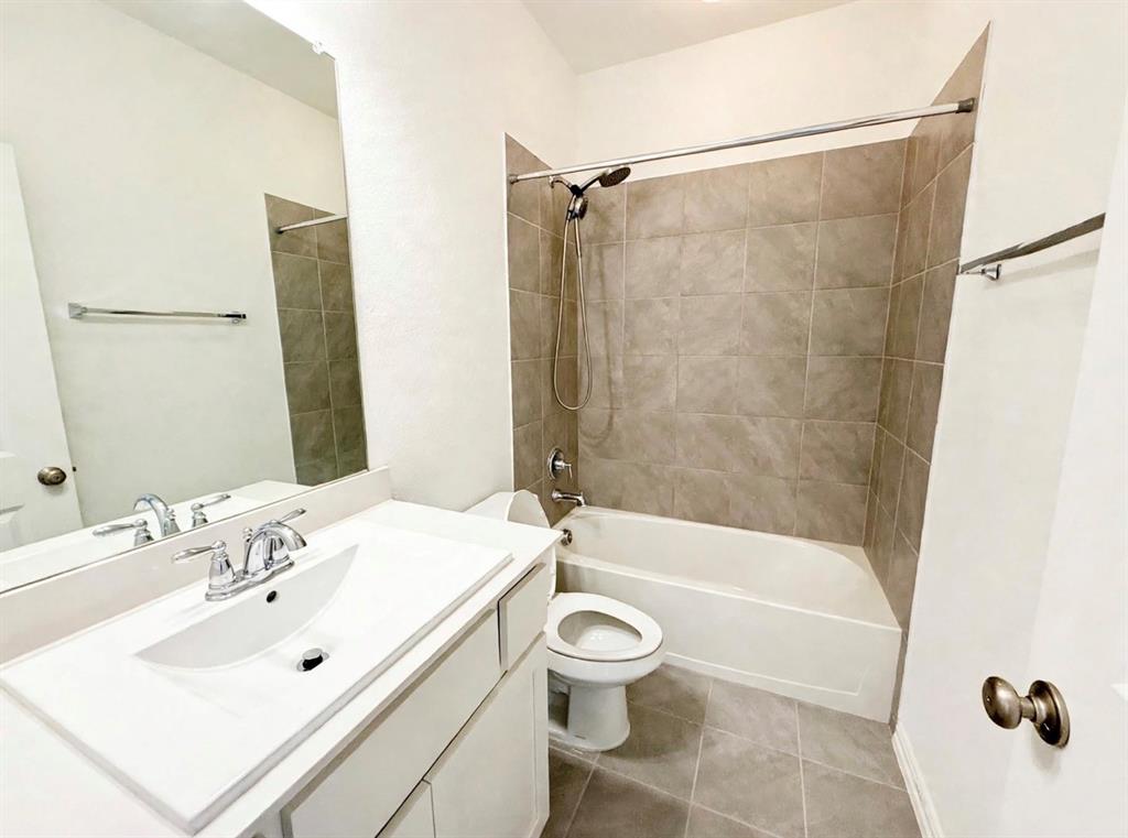 Bathroom featuring a vanity with an integrated basin, large wall-mounted mirror, ceramic tile flooring, and a tub-shower combination with full-height tile surround