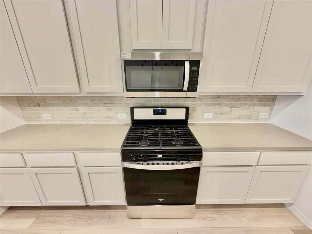 Kitchen featuring shaker-style cabinetry, solid-surface countertops, horizontal tile backsplash, stainless steel gas range, and built-in microwave