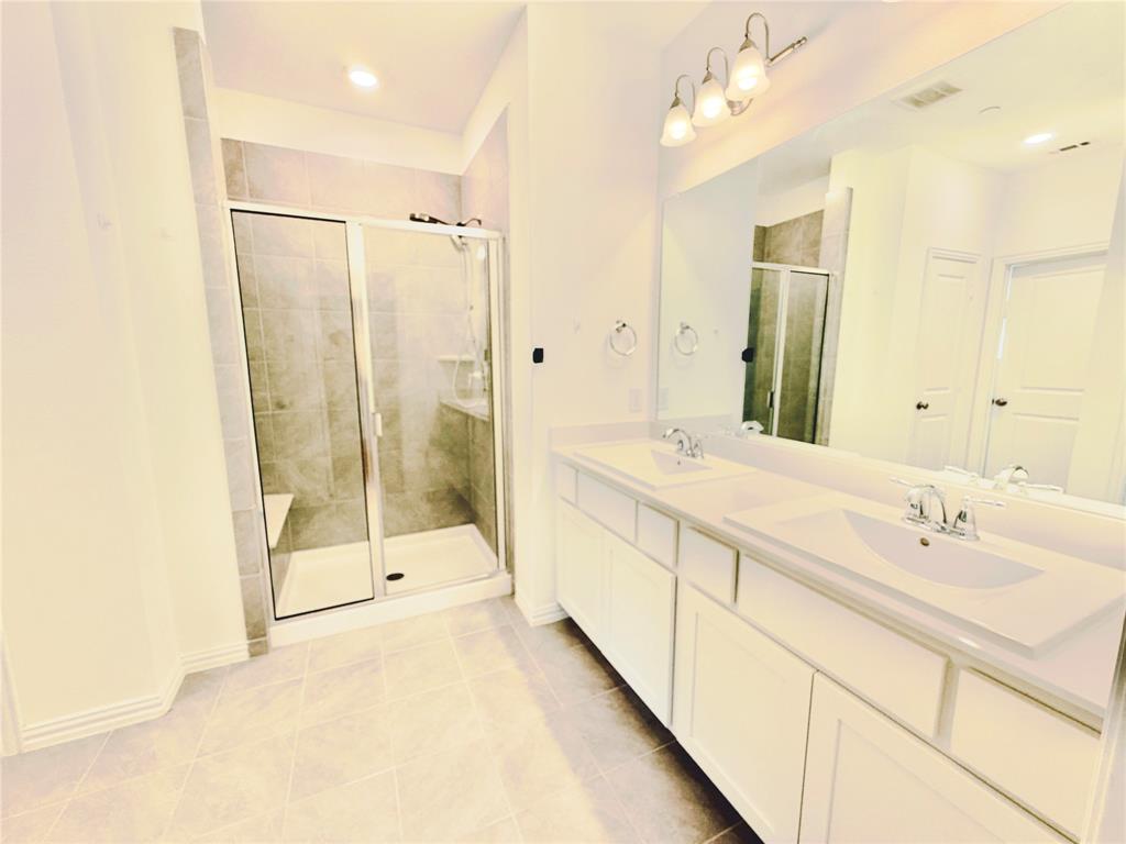 Dual vanity with integrated sinks, stone-finish countertops, glass-enclosed shower featuring tiled surround, and full-width wall mirror