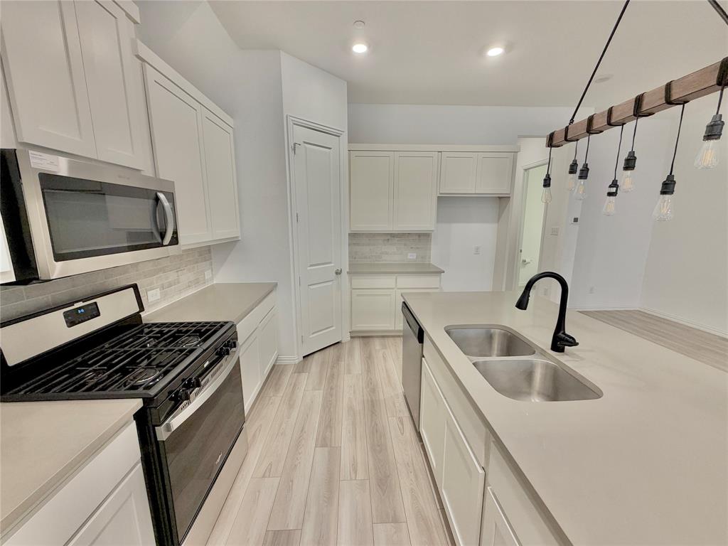 Kitchen featuring white cabinetry, solid-surface countertops, wood-finish flooring, a stainless steel gas range with overhead microwave, and a center island with a dual-basin sink and matte black faucet