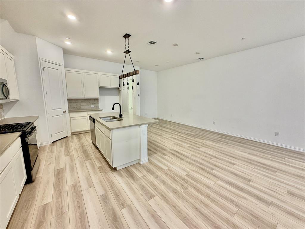 Kitchen featuring wood-finish flooring, a central island with a solid surface countertop, matte black faucet, and pendant lighting