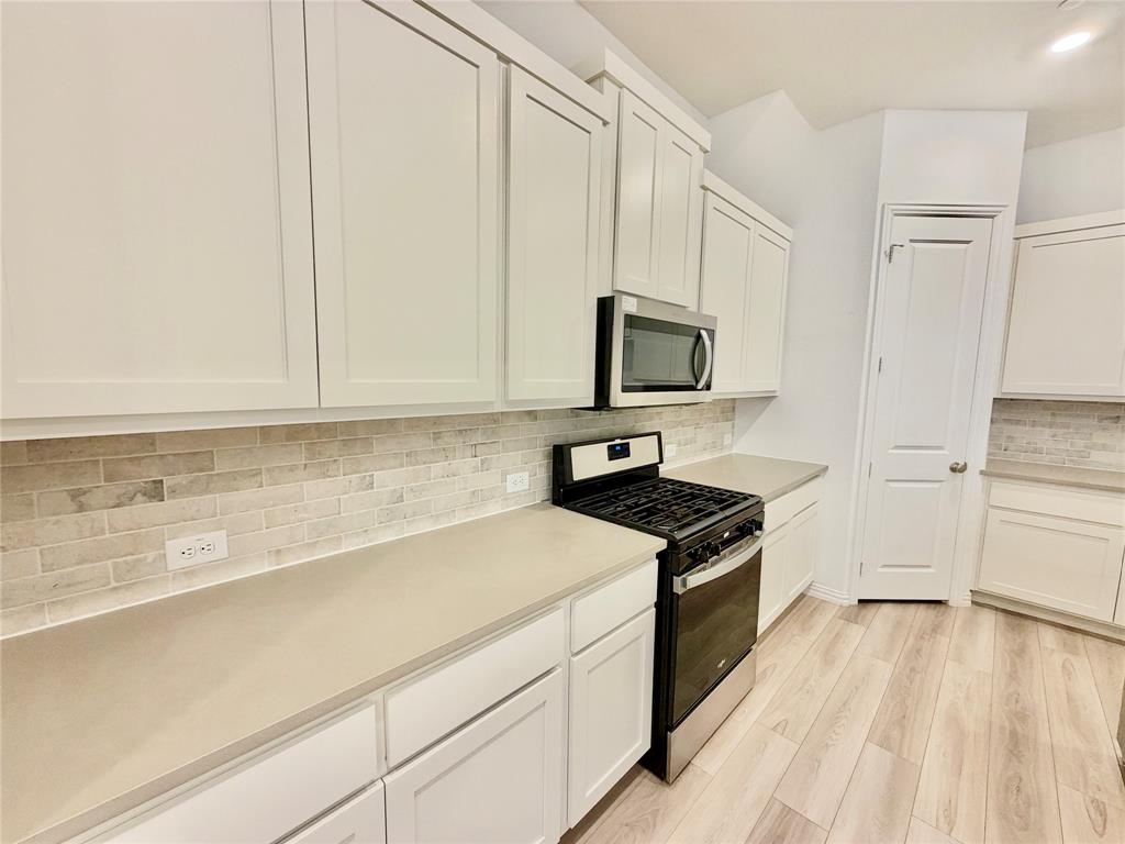 Kitchen featuring white shaker-style cabinetry, neutral-toned stone-finish countertops, subway tile backsplash, stainless steel microwave, and wood-finish flooring