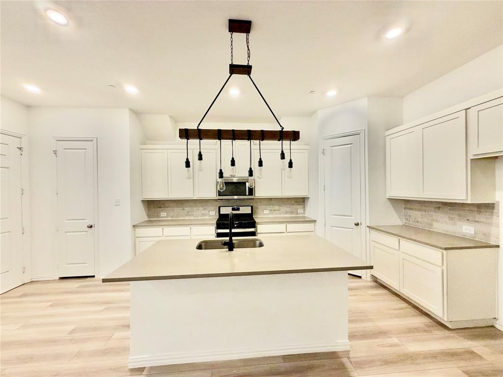 Kitchen featuring an island with a dual-basin sink, light-toned countertops, shaker-style cabinetry, a tile backsplash, and a multi-light wooden beam chandelier