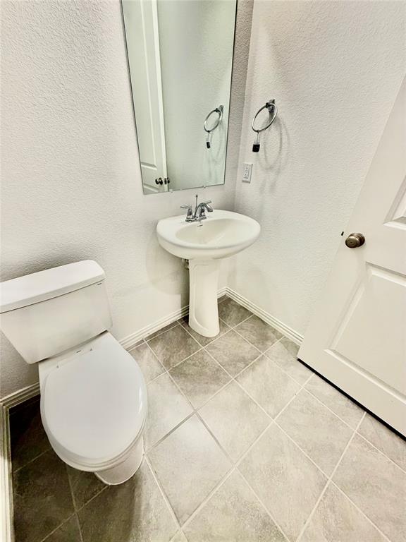 Pedestal sink with a two-handle chrome faucet, rectangular wall-mounted mirror, ceramic tile flooring, and a two-piece white toilet