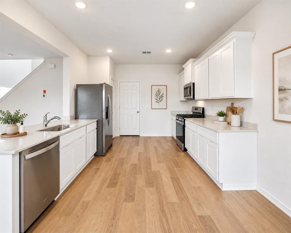 Kitchen featuring white cabinetry, quartz countertops, stainless steel appliances, and wood-finish flooring