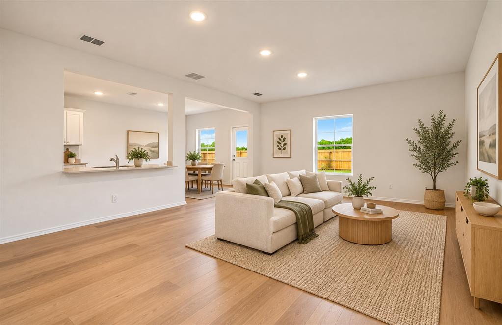 Open-concept interior featuring light wood-finish flooring, recessed lighting, neutral wall paint, and a stone-topped kitchen breakfast bar