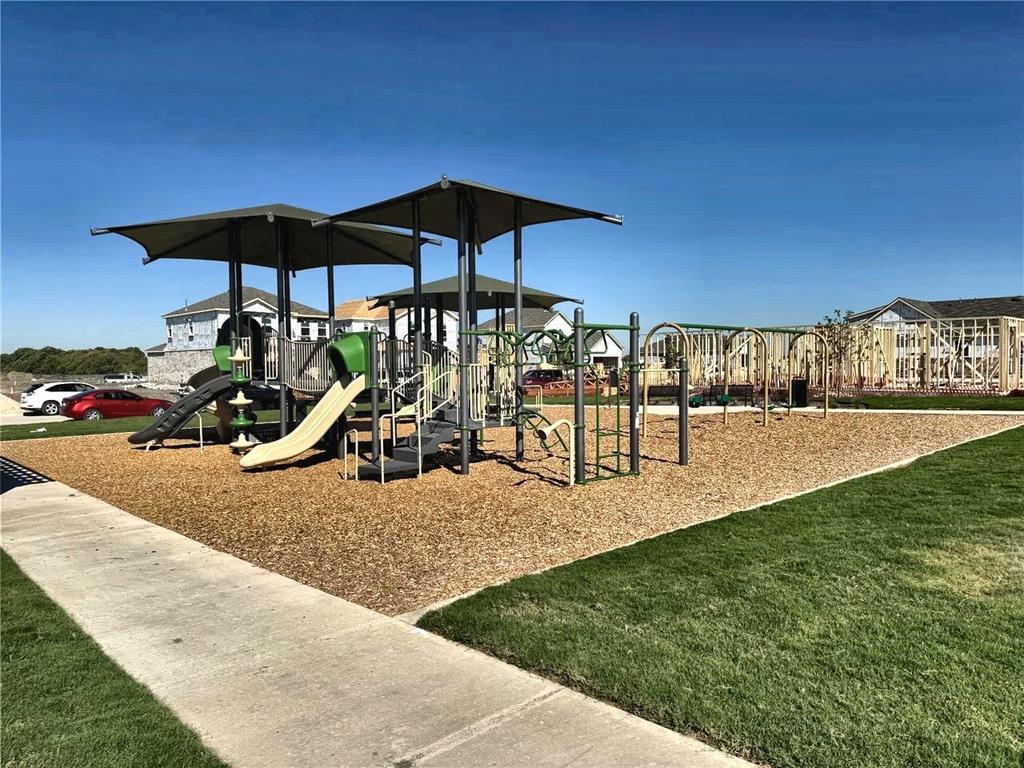 Community recreational area featuring a multi-structure playground, shade canopies, climbing apparatus, and slides, surrounded by landscaped turf and a paved walking path